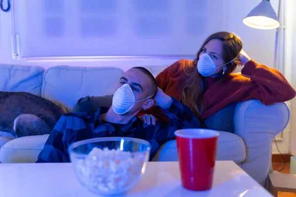 Coronavirus. A couple sitting on a sofa on a quarantine at home making a video call with the tablet. Couple at home on the couch, both wear masks because of avoiding contagion.
