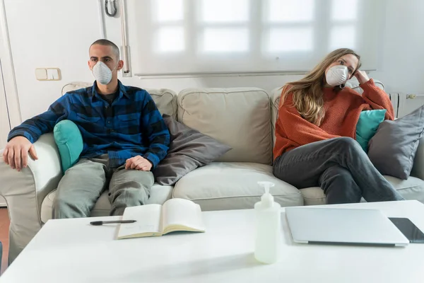 Coronavirus 一对夫妇坐在沙发上 在家里的隔离室里看电视 夫妻二人在家里沙发上 都戴着口罩 以免传染 呆在家里 — 图库照片
