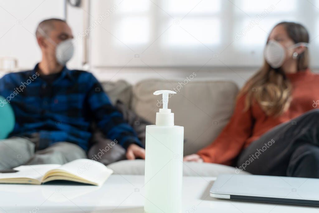 Coronavirus. A couple sitting on a sofa on a quarantine at home watching tv. Couple at home on the couch, both wear masks because of avoiding contagion. Stay at home. 