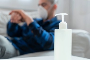 Coronavirus. Evde koruyucu maske takan bir adam. Koronavirüs yüzünden karantinaya alınan kadın ellerini dezenfektan jeliyle temizliyor. Evden çalışıyorum. Ellerini dezenfektan jeliyle temizle.. 