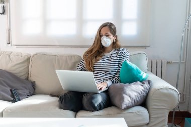 Coronavirus. Woman at home wearing protective mask. Woman in quarantine for coronavirus on the couch cleaning her hands with sanitizer gel. Working from home. Clean your hands with sanitizer gel.  clipart