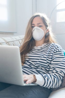 Coronavirus. Woman at home wearing protective mask. Woman in quarantine for coronavirus on the couch cleaning her hands with sanitizer gel. Working from home. Clean your hands with sanitizer gel.  clipart