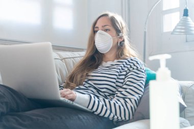 Coronavirus. Evde koruyucu maske takan bir kadın. Koronavirüs yüzünden karantinaya alınan kadın ellerini dezenfektan jeliyle temizliyor. Evden çalışıyorum. Ellerini dezenfektan jeliyle temizle.. 