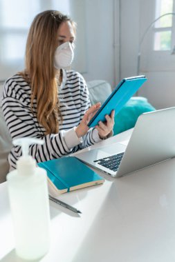 Coronavirus. Evde koruyucu maske takan bir kadın. Koronavirüs yüzünden karantinaya alınan kadın ellerini dezenfektan jeliyle temizliyor. Evden çalışıyorum. Ellerini dezenfektan jeliyle temizle.. 