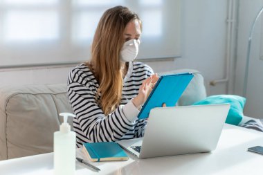Coronavirus. Evde koruyucu maske takan bir kadın. Koronavirüs yüzünden karantinaya alınan kadın ellerini dezenfektan jeliyle temizliyor. Evden çalışıyorum. Ellerini dezenfektan jeliyle temizle.. 