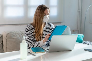 Coronavirus. Evde koruyucu maske takan bir kadın. Koronavirüs yüzünden karantinaya alınan kadın ellerini dezenfektan jeliyle temizliyor. Evden çalışıyorum. Ellerini dezenfektan jeliyle temizle.. 