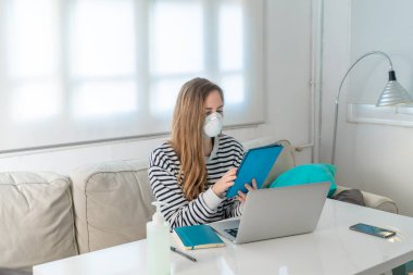 Coronavirus. Evde koruyucu maske takan bir kadın. Koronavirüs yüzünden karantinaya alınan kadın ellerini dezenfektan jeliyle temizliyor. Evden çalışıyorum. Ellerini dezenfektan jeliyle temizle.. 
