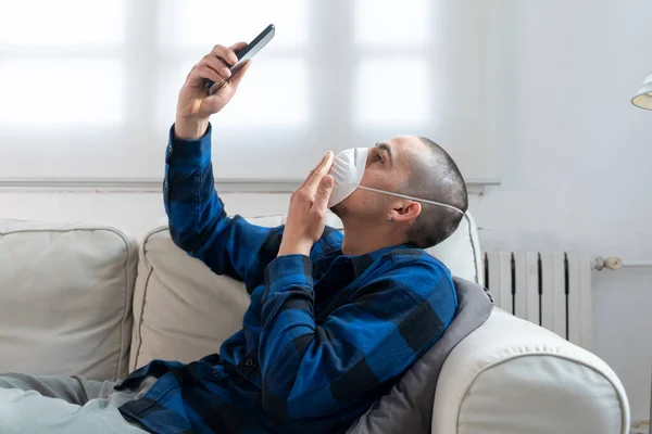 Coronavirus. Man at home wearing protective mask. Woman in quarantine for coronavirus on the couch cleaning her hands with sanitizer gel. Working from home. Clean your hands with sanitizer gel.