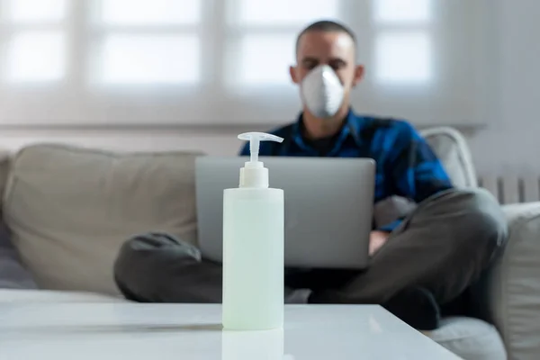 Coronavirus. Man at home wearing protective mask. Woman in quarantine for coronavirus on the couch cleaning her hands with sanitizer gel. Working from home. Clean your hands with sanitizer gel.