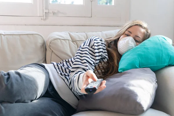 Coronavirus. Woman at home wearing protective mask. Woman in quarantine for coronavirus on the couch cleaning her hands with sanitizer gel. Working from home. Clean your hands with sanitizer gel.