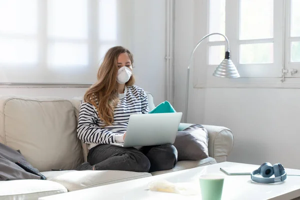 Coronavirus. Woman at home wearing protective mask. Woman in quarantine for coronavirus on the couch cleaning her hands with sanitizer gel. Working from home. Clean your hands with sanitizer gel.