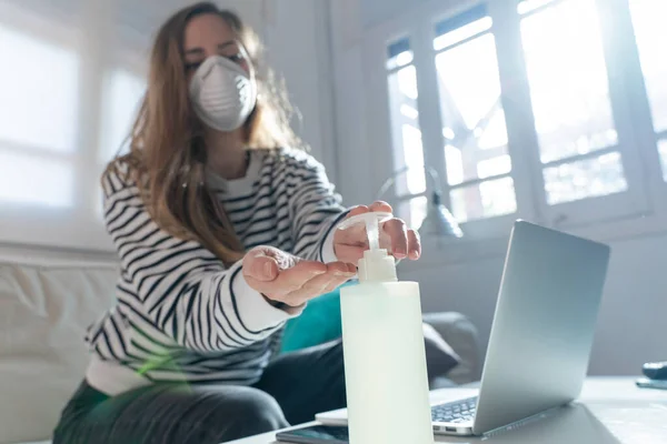 Coronavirus. Woman at home wearing protective mask. Woman in quarantine for coronavirus on the couch cleaning her hands with sanitizer gel. Working from home. Clean your hands with sanitizer gel.