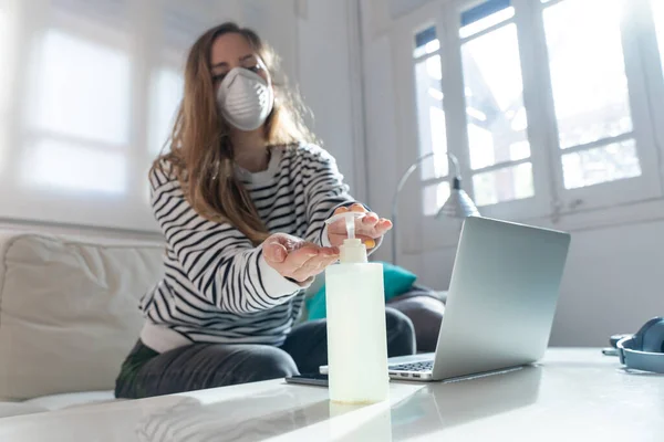 Coronavirus. Woman at home wearing protective mask. Woman in quarantine for coronavirus on the couch cleaning her hands with sanitizer gel. Working from home. Clean your hands with sanitizer gel.