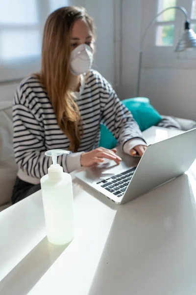 Coronavirus. Woman at home wearing protective mask. Woman in quarantine for coronavirus on the couch cleaning her hands with sanitizer gel. Working from home. Clean your hands with sanitizer gel.