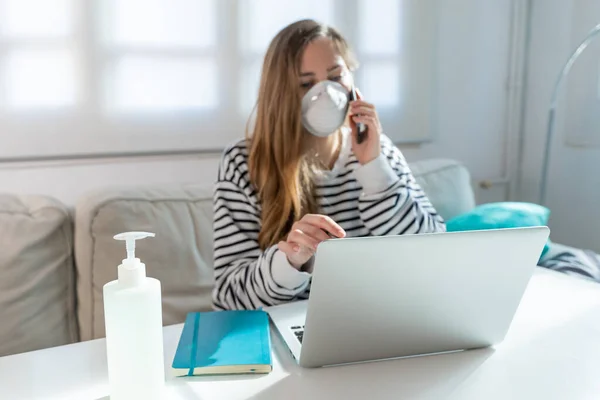 Coronavirus. Woman at home wearing protective mask. Woman in quarantine for coronavirus on the couch cleaning her hands with sanitizer gel. Working from home. Clean your hands with sanitizer gel.