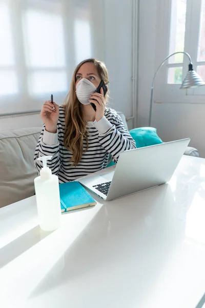 Coronavirus. Woman at home wearing protective mask. Woman in quarantine for coronavirus on the couch cleaning her hands with sanitizer gel. Working from home. Clean your hands with sanitizer gel.