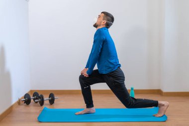 Coronavirus. COVID-19. Karantina sırasında maskeli genç adam evde spor yapıyor. Ev aktivitelerinde kal. Pandemiden enfeksiyonu önlemek için. Evde sağlıklı.. 