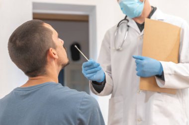 Coronavirus testi. Hasta bakımı. Teşhisler. Doktor evde sağlıksız bir adamı ziyaret ediyor, koronavirüs testi. Doktor muayenehanesinde oturan hastaya danışmanlık yapıyor. Önlem için yüz maskesi ve lastik eldivenler.. 