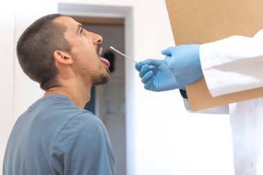 Coronavirus testi. Hasta bakımı. Teşhisler. Doktor evde sağlıksız bir adamı ziyaret ediyor, koronavirüs testi. Doktor muayenehanesinde oturan hastaya danışmanlık yapıyor. Önlem için yüz maskesi ve lastik eldivenler.. 