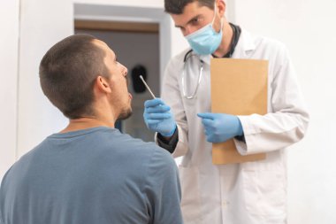 Coronavirus. Hasta bakımı. Teşhisler. Doktor evde sağlıksız bir adamı ziyaret ediyor, koronavirüs testi. Doktor muayenehanesinde oturan hastaya danışmanlık yapıyor. Önlem için yüz maskesi ve lastik eldivenler.. 