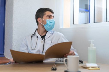 Coronavirus. Doktor teşhis üzerinde çalışıyor. Coronavirüs salgını sırasında reçeteyi hastanenin masasına yazıyor. Önlem için yüz maskesi ve dezenfektan jeli. Sağlık çalışanları. Coronavirus testi. 