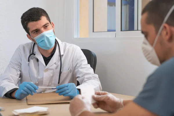 Coronavirus. Patient care. Diagnostics. Doctor visiting unhealthy man at home, coronavirus test. Doctor consults patient sitting at doctor office. Face mask and rubber gloves for prevention.