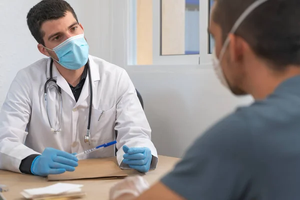 Coronavirus. Patient care. Diagnostics. Doctor visiting unhealthy man at home, coronavirus test. Doctor consults patient sitting at doctor office. Face mask and rubber gloves for prevention.