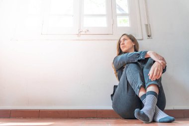 Yalnız genç bir kadın, boş bir odada baş başa otururken bunalımda ve stresli. Ev endişesi. Olumsuz duygu konsepti. Coronavirus. Karantina sırasında izole edilmiş Corona virüsü hastası bir kadın. Üzgün kadın..