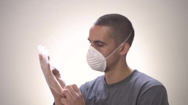 Coronavirus konsepti. COVID-19. Beyaz arka planda koruma maskesi olan genç bir adam. Koruma maskesini yavaş çekime alıyorum. Evde izole edilmiş. Hapis cezasına çarptırıldı. Sosyal uzaklık. Grip..