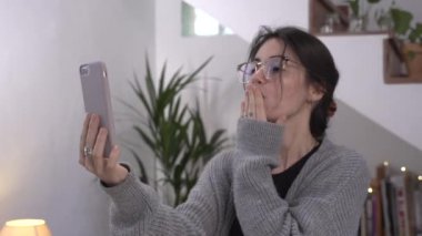 Evde bir kadın var ve koltukta cep telefonu kullanıyor. Görüntülü arama. Cep telefonuyla video konferansı. Ailesi ve arkadaşlarıyla konuşuyor. Öptüm