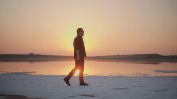 Молодой человек, гуляющий по озеру на закате — стоковое видео