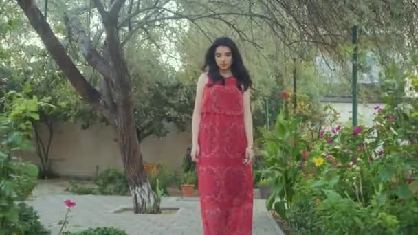 Mooi meisje in rode jurk wandelingen alleen in de groene tuin — Stockvideo