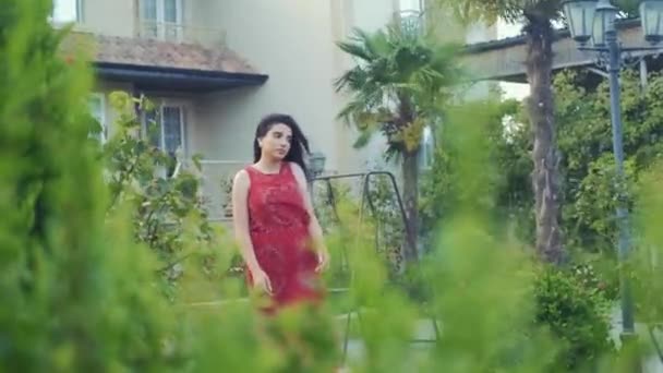 穿着红衣的漂亮女孩独自在绿色的花园里散步 — 图库视频影像