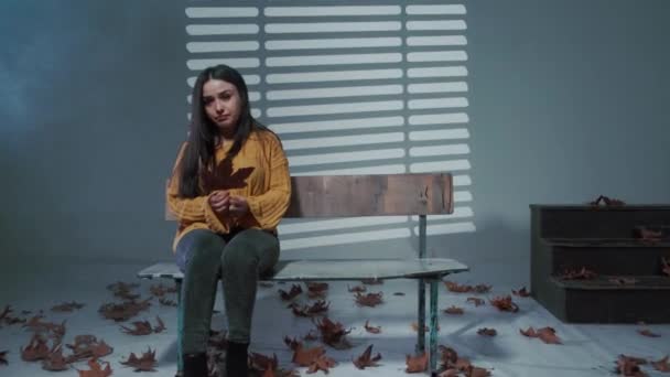 Jong verdrietig kijken naar camera, zitten op een bank met een bloemblaadje in handen — Stockvideo