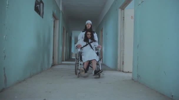 Žena sestra tlačí pacienta v invalidním vozíku přes nemocniční chodbu — Stock video