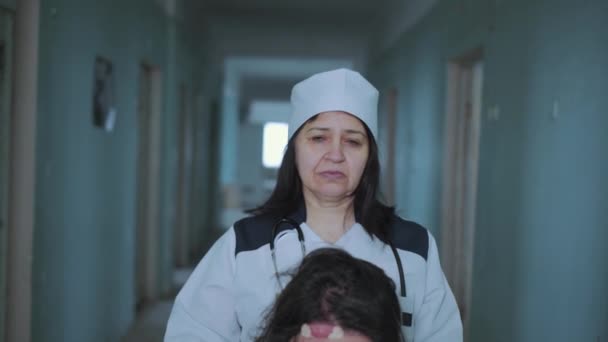 Pielęgniarka popycha pacjentkę na wózku inwalidzkim korytarzem szpitalnym. — Wideo stockowe