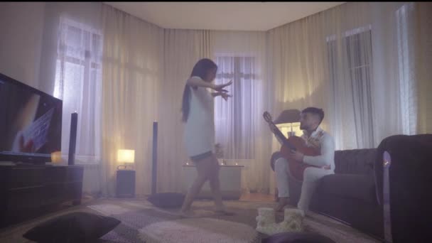 Гитарист играет для девушки, танцующей в ночной комнате — стоковое видео