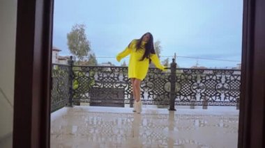 Güzel kız balkonda dikilip zehirleyen kameraya bakıyor.