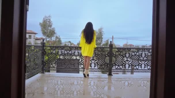 Beautiful girl stands on the balcony looking at the camera poising — Stock Video