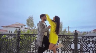 Genç çift ayakta duruyor ve nazikçe balkonda sarılıyor.