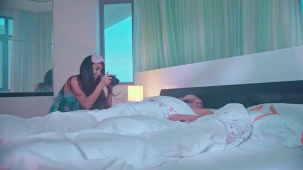 Το κορίτσι ξύπνησε έναν κοιμισμένο άντρα το πρωί στην κρεβατοκάμαρα βγάζει μια φωτογραφία Όμορφο ζευγάρι που φιλιέται στο κρεβάτι — Αρχείο Βίντεο