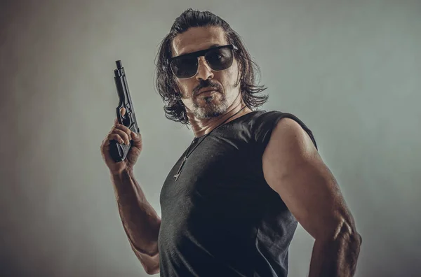 Genç bir adamın elinde silah gözlerinde siyah gözlüklerle seksi kaslı portresi..