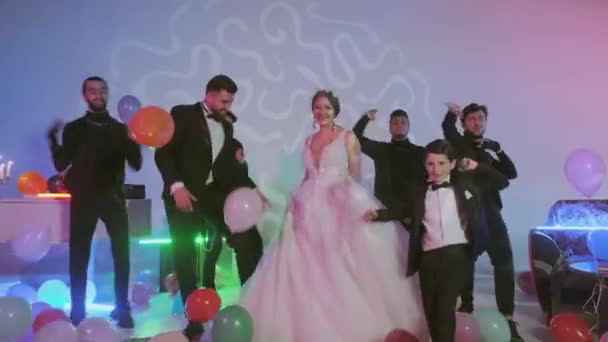 結婚式のパーティーでお客様と一緒に踊る幸せな新郎新婦、床に多色のボール、カラフルなネオンで飾られた部屋. — ストック動画