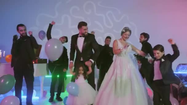 Novio feliz y novia bailando con los invitados en la fiesta de bodas, bolas multicolores en el suelo, habitación con decoradas con luces de neón de colores . — Vídeo de stock