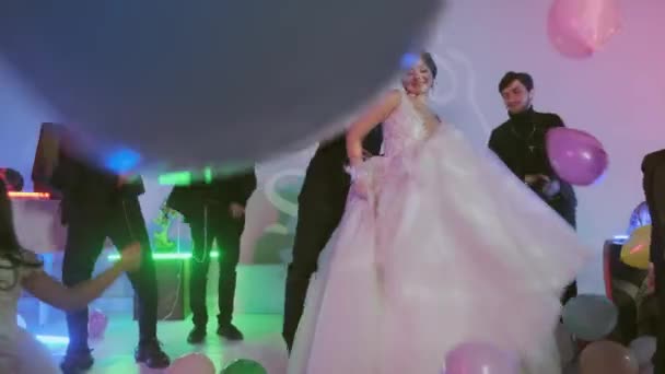 Счастливый жених и невеста танцы с гостями на свадьбе, разноцветные шары на полу, комната с украшенной красочными неоновыми огнями . — стоковое видео