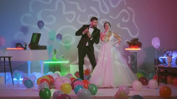 Krásná nevěsta v svatební závoj a hosté tančí na svatbě.Krásná modelka dívka v bílých svatebních šatech, multi-barevné vzduchové balónky na podlaze, pokoj s zdobené barevnými neonovými světly — Stock video