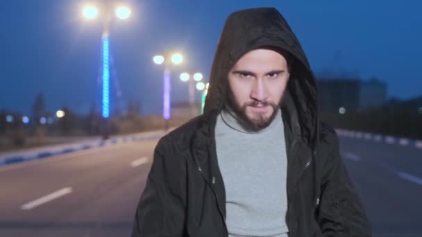 Mladý muž kapuce chůze na osvětlené městské ulici v noci — Stock video