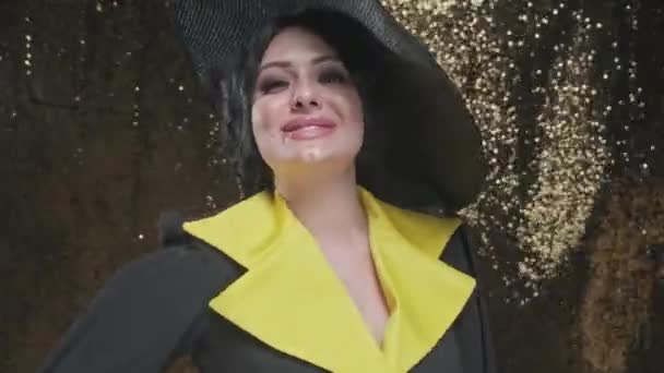 Portré elegáns gyönyörű nő fekete ruhában és széles kalap elszigetelt arany háttér stúdió — Stock videók