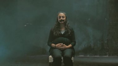 Yüzünde morluklar ve kan olan genç bir kadın. Aile içi şiddet, kameraya bakmak ve ağlamak, ağzı siyah bantla kaplı, karanlık bir sorgu odasında oturuyor.
