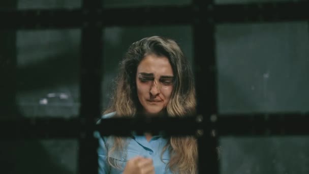 Молода жінка з синцями і кров'ю на обличчі. Домашнє насильство, дивиться на камеру і плаче, за ґратами у в'язниці . — стокове відео